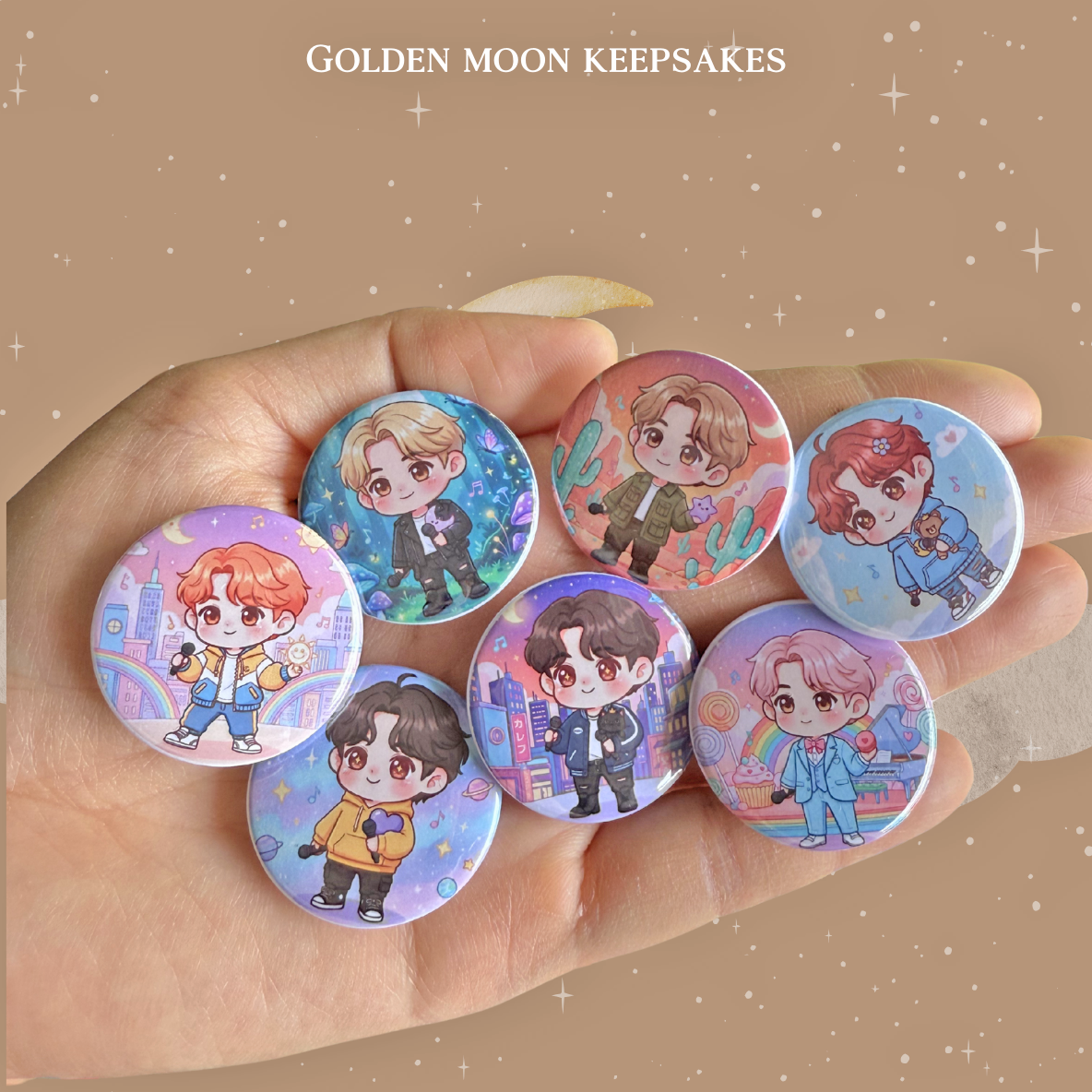 A hand holding seven 1.25-inch glossy button pins, each featuring a unique chibi-style character illustration. The characters are depicted in various colorful settings, including vibrant cityscapes with rainbows, desert landscapes with cacti, and starry galaxy backgrounds. The image is centered on a tan background with white stars and the text "GOLDEN MOON KEEPSAKES" at the top.