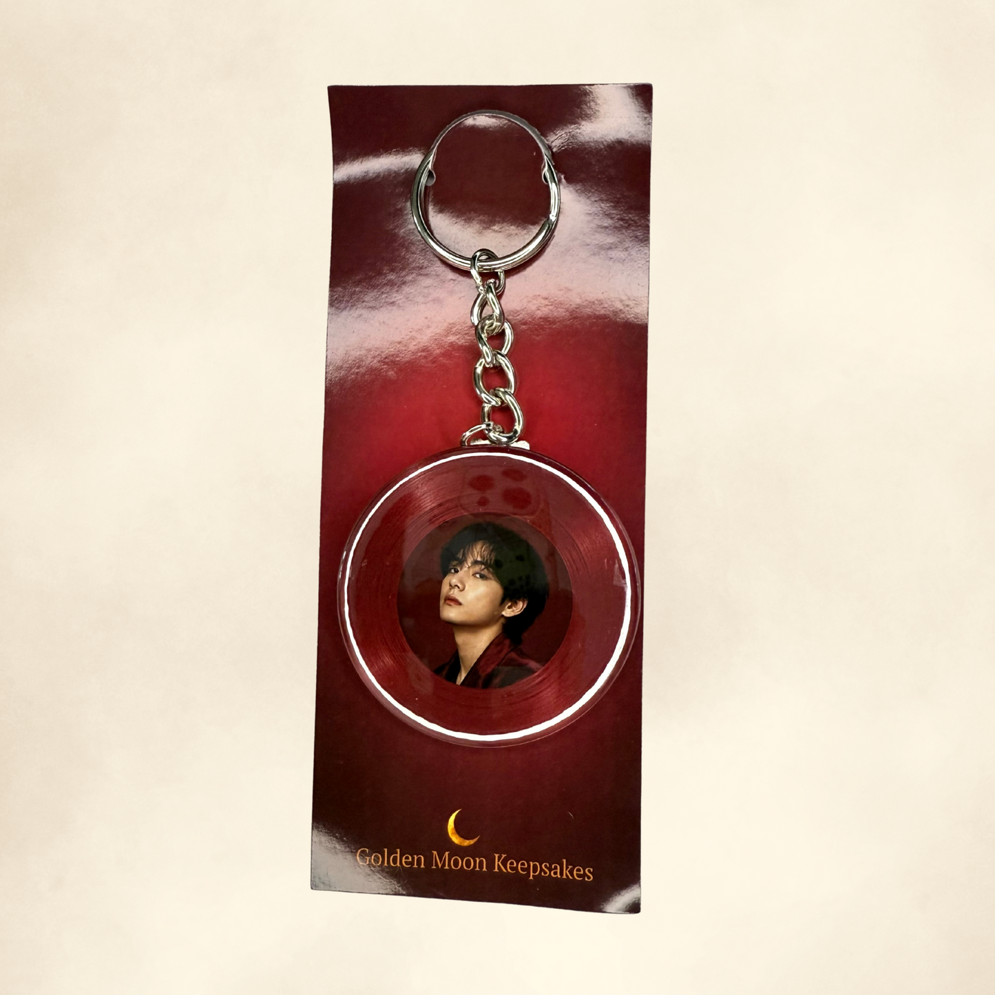 Keychain with a circular design featuring a person's face, displayed on a red card with 'Golden Moon Keepsakes' text.