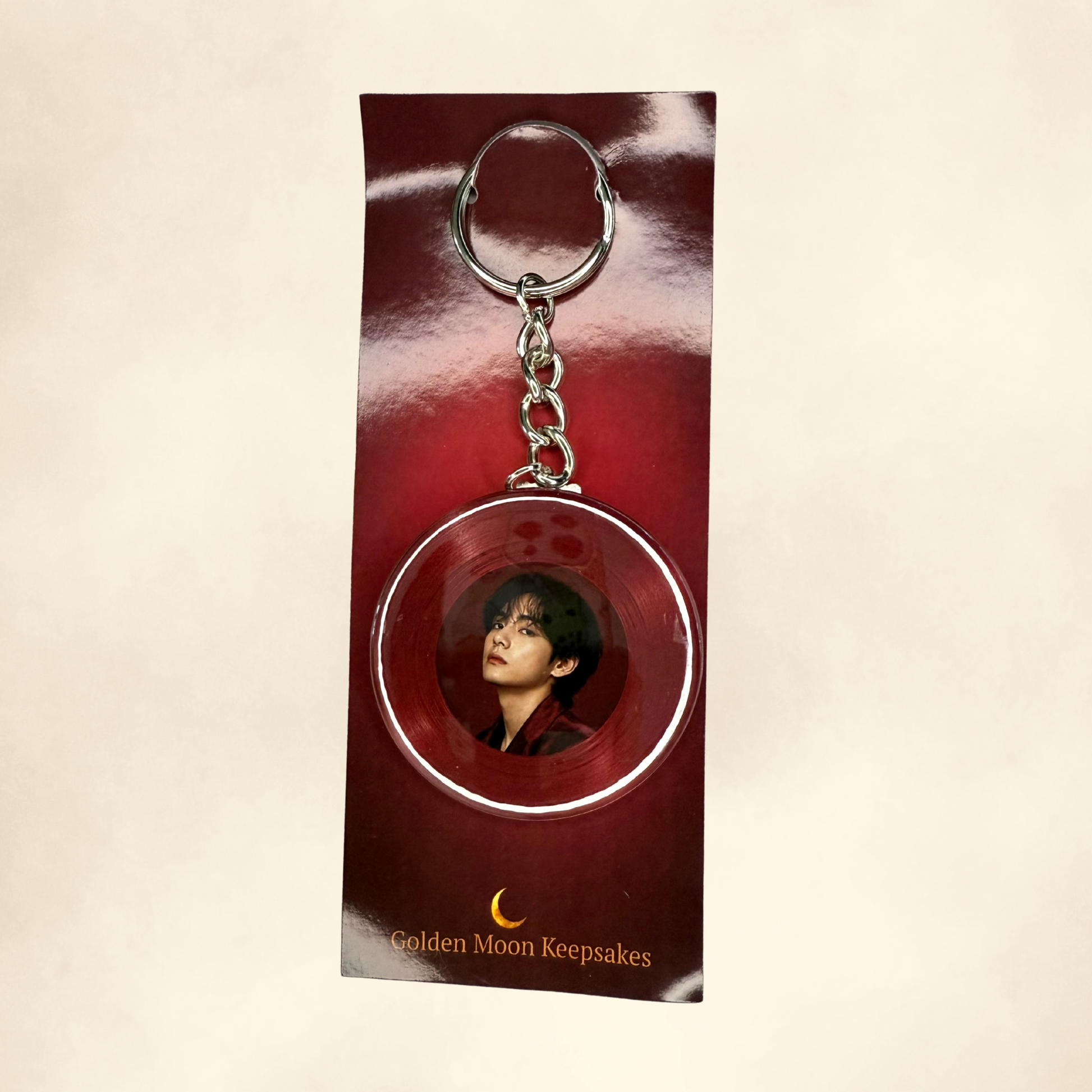 Keychain with a circular design featuring a person's face, displayed on a red card with 'Golden Moon Keepsakes' text.