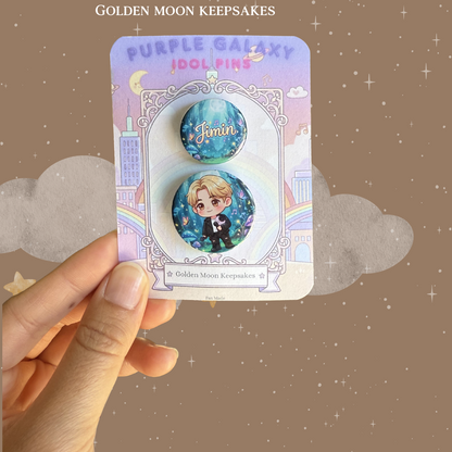 A two-piece pin set displayed on a "Golden Moon Keepsakes" card. The larger pin features a chibi character with blonde hair in a galaxy-inspired setting with stars and butterflies. The smaller coordinating pin displays the name "Jimin" in an elegant script over a deep blue and purple nebula background.