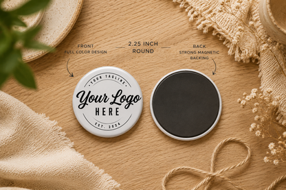 Two round magnetic tin badges shown on a wooden surface with decorative fabric and dried flowers. One badge is white with black placeholder text reading 'Your Logo HERE' and 'Fresh Tabulary Est.