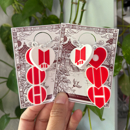 Two red and white heart-shaped earrings held in front of a green plant.